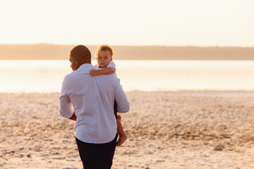 Young african american father walking on the beach with his toddler son. baby boy on father hands