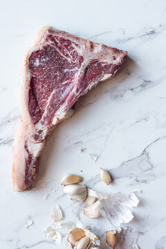 raw beef t-bone steak with garlic cloves on a marble background