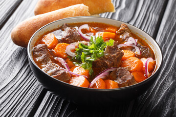 Bo Kho beef ragout in spicy sauce with carrots served with Vietnamese bread close-up in a bowl on the table. horizontal