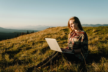 Hipster woman working with laptop sitting in mountains. Hiker tourist enjoying valley view sunset....