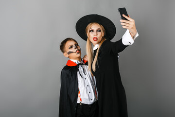 A boy and a girl in Halloween costumes take a selfie on a gray wall background