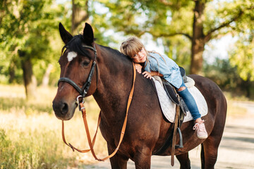 Cute little girl with long hair riding a horse outdoors. Pet therapy