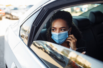 Woman wearing a medical mask on a business travel around the city checking her mobile phone, chatting and calling. Business trips during pandemic, new normal and coronavirus travel safety concept. © Konstantin Zibert