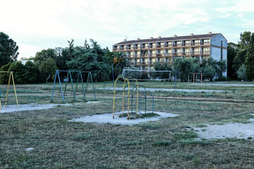 Old playground with metal swings by abandoned hotel