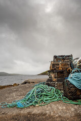 Stack of used fishing traps and lines ashore on a pier. Cloudy grey low clouds, Fish industry concept.