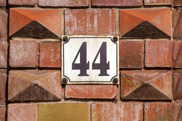 Weisses Hausnummernschild Nr. 44 auf r&ouml;tlicher Backsteinmauer, Deutschland, Europa