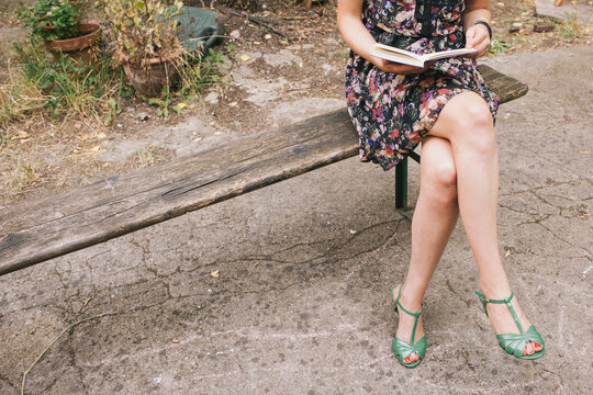 Young woman, sitting on a beanch in a back yard, reading a book.