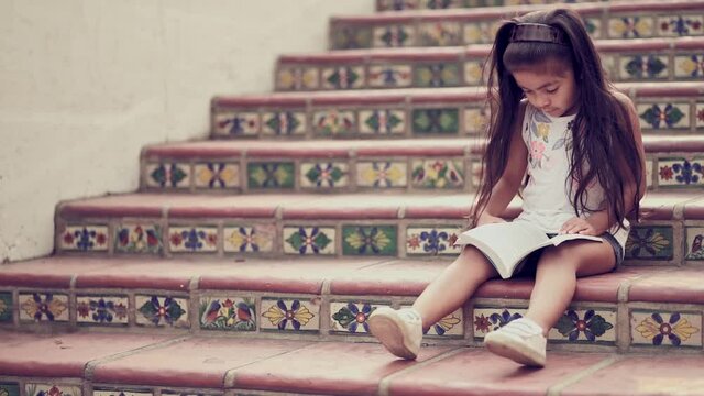 Young girl sitting on terracotta staircase reading a book