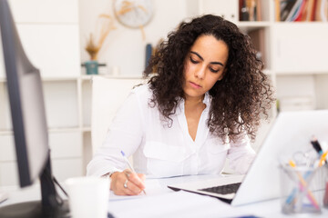 Portrait of young female business employee writing and working with laptop at office