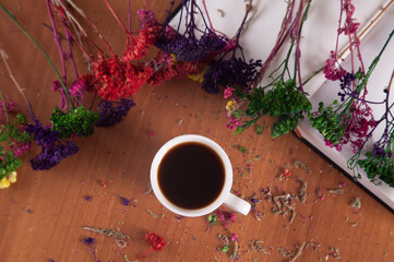 Colorful flowers and a cup of coffee with a book on a wooden background.