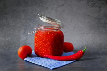 Ground hot red pepper with tomatoes in a glass jar on a dark background. A spicy seasoning made from pepper and tomatoes at home. Home cooking.