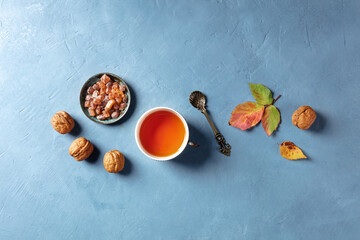 A flat lay autumn composition with a cup of tea, nuts, and vibrant fall leaves, shot from the top on a blue background with a place for text