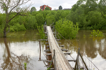 Fototapeta premium Rustic suspension footbridge across the river during flood after rains