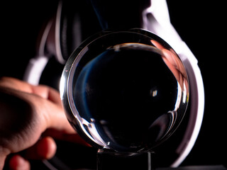 hand with a cannabis cigar and white headphones playing with its reflection in a crystal ball on a black background . Music and cannabis concept