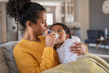 Lovely mother embracing daughter making inhalation with a nebulizer