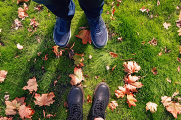 Male and female legs in sneakers and boots standing on ground with yellow autumn leaves