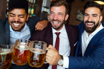 Handsome businessmen are drinking beer, talking and smiling while resting at the pub