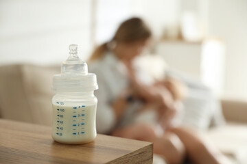 Mother breastfeeding her little baby at home, focus on bottle with milk. Healthy growth