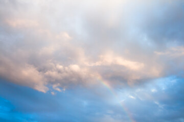 Naklejka na ściany i meble A shy rainbow breaks through a cluster of clouds after a rainy day
