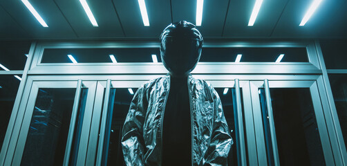 Futuristic scene with person with black helmet/mask and silver jacket with neons iluminating around.