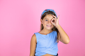 Young beautiful child girl over isolated pink background doing ok gesture shocked with smiling face, eye looking through fingers