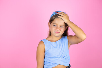 Young beautiful child girl over isolated pink background putting one hand on her head smiling like she had forgotten something