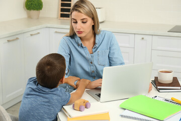 Obraz premium Little boy bothering mother at work in kitchen. Home office concept