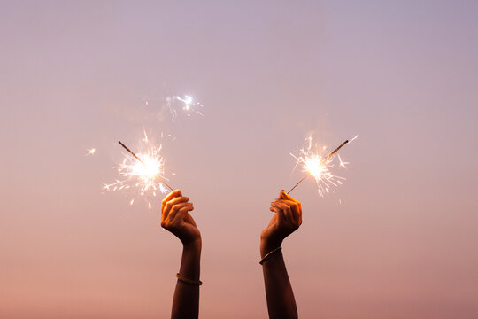 Woman's hand holding sparkler to the sky at twilight