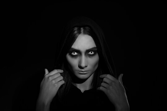 Mysterious witch with spooky eyes on dark background. Black and white effect