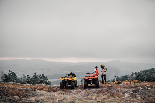 Two friends standing on the cliff next to quadro motorcycles