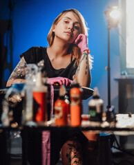 Seductive looking female tattoo master posing in her small but modern studio with spotlight and...