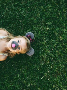young girl with mouse ears and nose on laying in grass