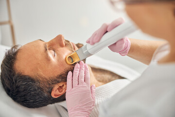 Esthetician removing unwanted hair from male cheek with laser device