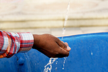     A dark-skinned hand catches a stream of water in his palm.