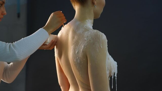 Crop artist applying wax on naked model