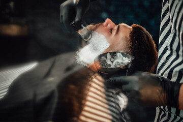 Modern and vintage barbershop with dark stylish brickwalls and barber which preparing his client for haircut.