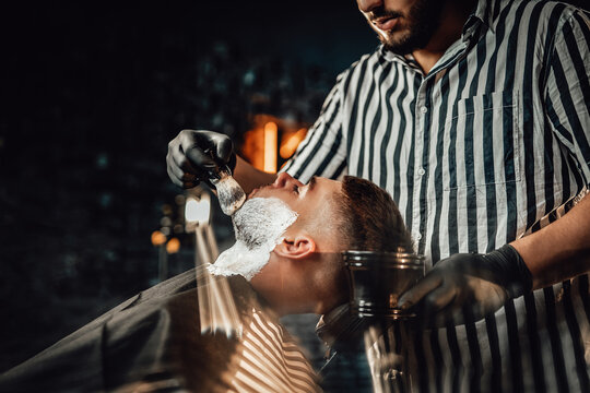 Modern and vintage barbershop with dark stylish brickwalls and barber which preparing his client for haircut.