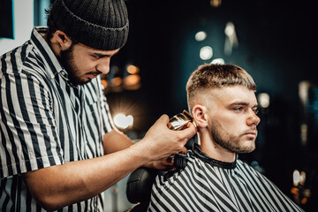 Professional barber cutting a guy in old fashioned hairstyle with modern clipper in his retro...