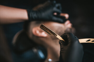 Adult guy is shaving by professional and skilled barber in stylish and modern saloon.