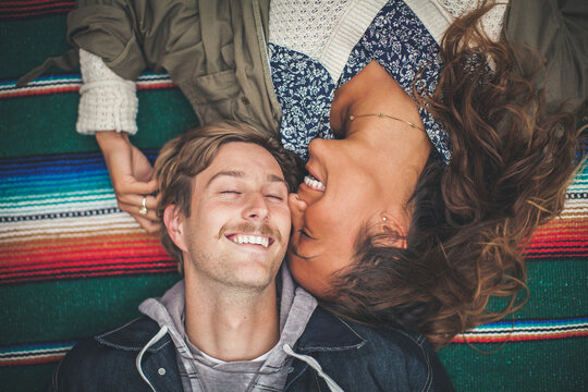 Young couple laying on colorful blanket and smiling.