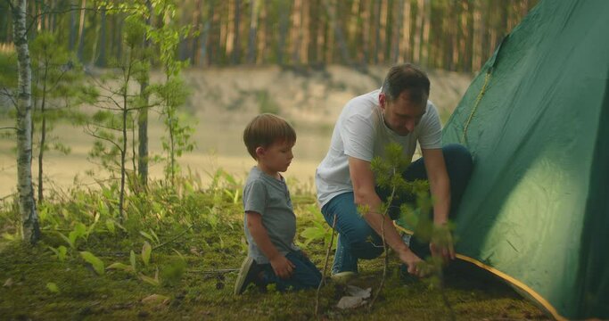 Tourists in the forest on the shore of the lake family father and son set up a tent camp in slow motion