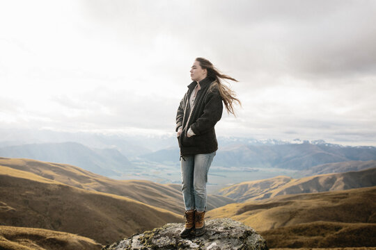 young woman standing on rock with mountains in background