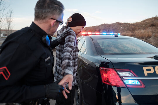 A Police Officer searching a suspect beside his cruiser.