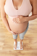 pregnancy, weight control and diet concept - close up of pregnant woman standing on scales at home