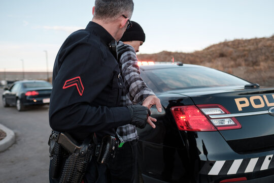A Police Officer searches a suspect next to his cruiser