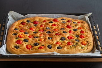 Freshly cooked focaccio lies on a baking sheet and stands on a black table.