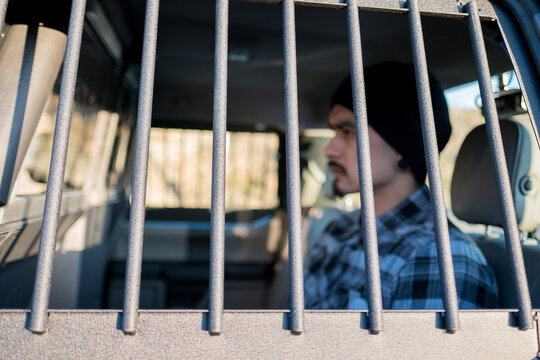 A man sits behind window bars in a police vehicle