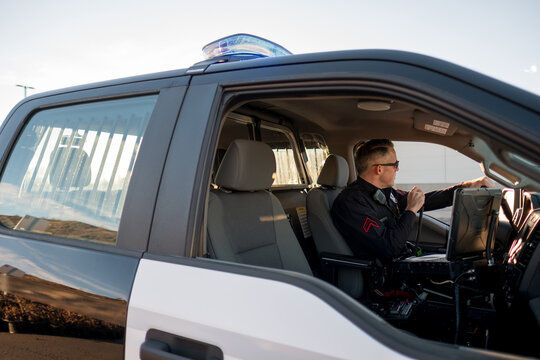 A Police Officer uses a radio while sitting in a police vehicle