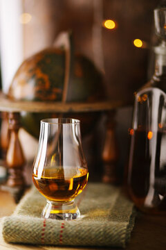 Whiskey glass with a pour of single malt whiskey and a decanter full of whiskey in the background.
