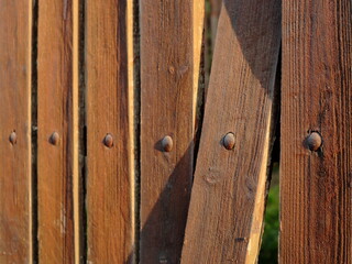 Close-up of a wooden fence with visible texture, nails, and warm sunlight highlighting the grain. One board is slightly misaligned, adding character to this rustic, handcrafted structure © Maciej Bonk